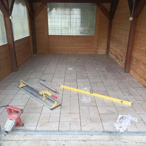 Fa szerkezetű kerti pavilon padlójának burkolása munka közben, csempevágóval